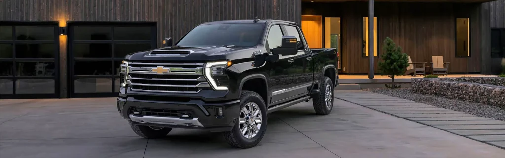 The image shows a black Chevrolet Silverado pickup truck parked in front of a modern home with a paved driveway.